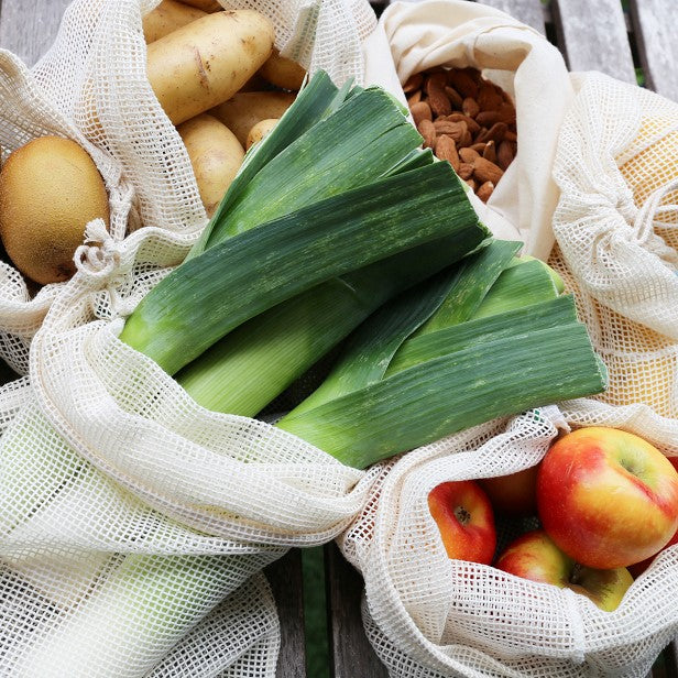 Bodegón de varias bolsas de rejilla con verduras, frutas, frutos secos y hortalizas dentro - LLevar & LLevar